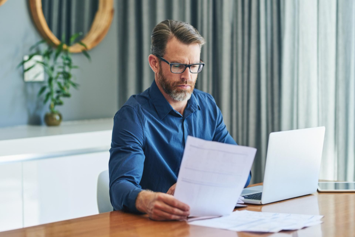 Empresário em escritório analisando documentos em frente ao notebook, representando riscos fiscais por omissão ou não emissão de nota fiscal.