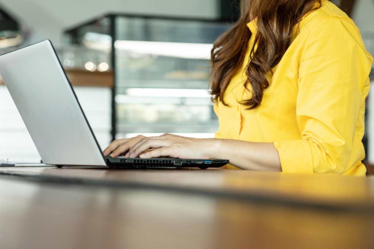 Mulher em ambiente de escritório sentada mexendo em seu notebook sobre uma mesa representando: CFOP 5101: guia completo da venda para comercialização.