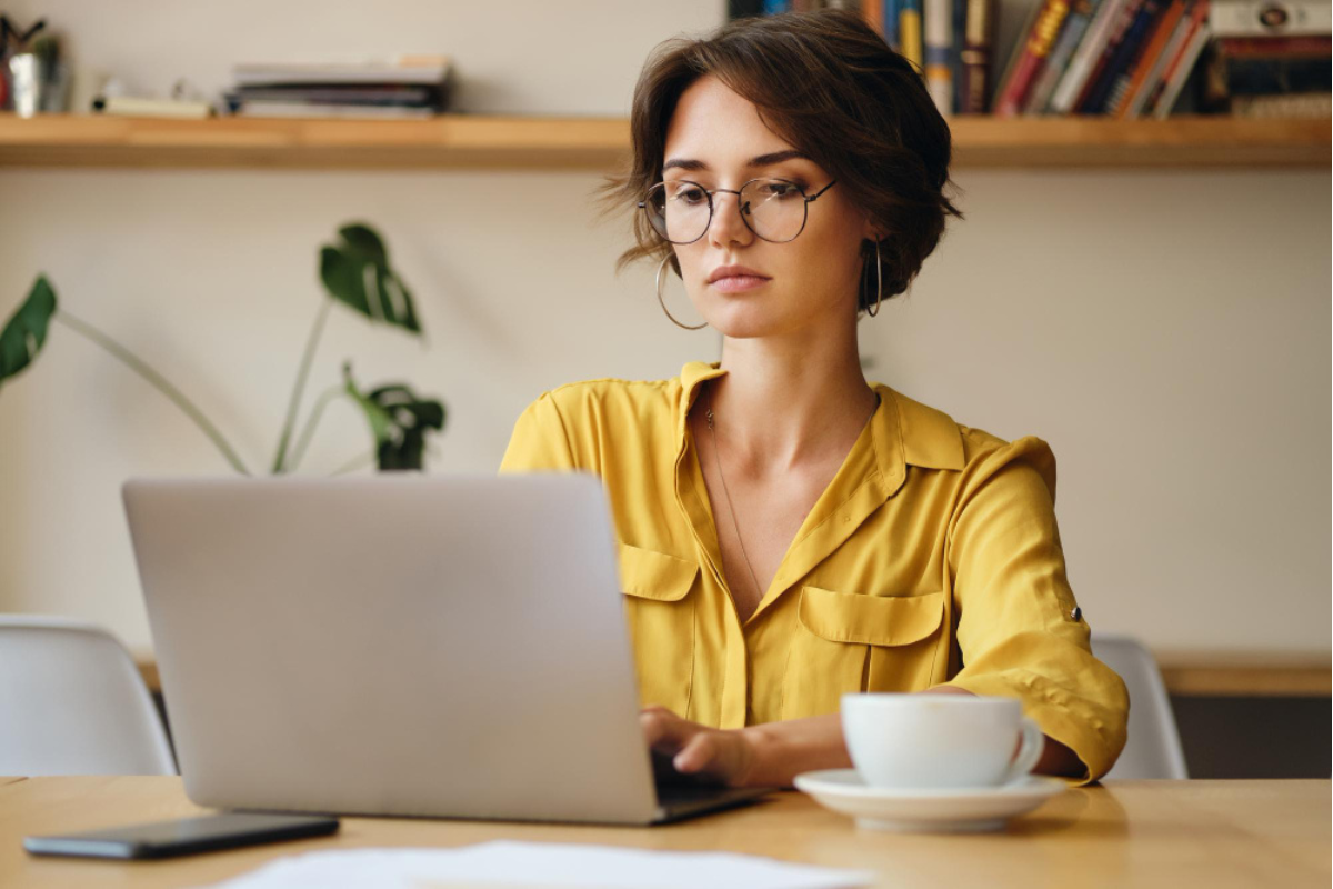 Mulher em ambiente de escritório sentada usando notebook sobre uma mesa com uma xícara com pires ao lado representando: CFOP 6106: venda de mercadoria sujeita ao regime de substituição tributária, cujo imposto já tenha sido retido anteriormente.