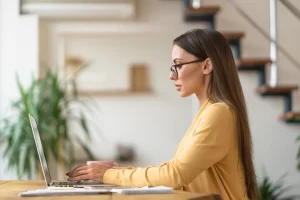 Mulher sentada usando notebook sobre uma mesa com caderno de anotações ao lado em ambiente de escritório representando: CFOP 6403: venda de mercadoria adquirida ou recebida de terceiros em operação com mercadoria sujeita ao regime de substituição tributária, na condição de contribuinte substituto.