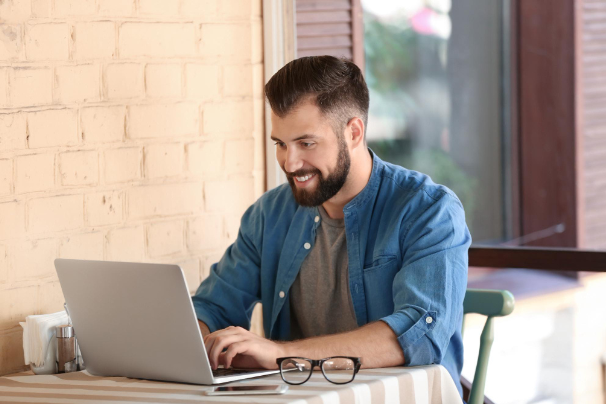 Homem sentado em ambiente de escritório usando um notebook sobra uma mesa com óculos ao lado: representando: CFOP 5901: remessa para industrialização por encomenda.