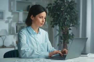 Mulher em ambiente de escritório sentada usando notebook sobre uma mesa representando: CFOP 6108: venda de mercadoria adquirida ou recebida de terceiros, destinada a não contribuinte.