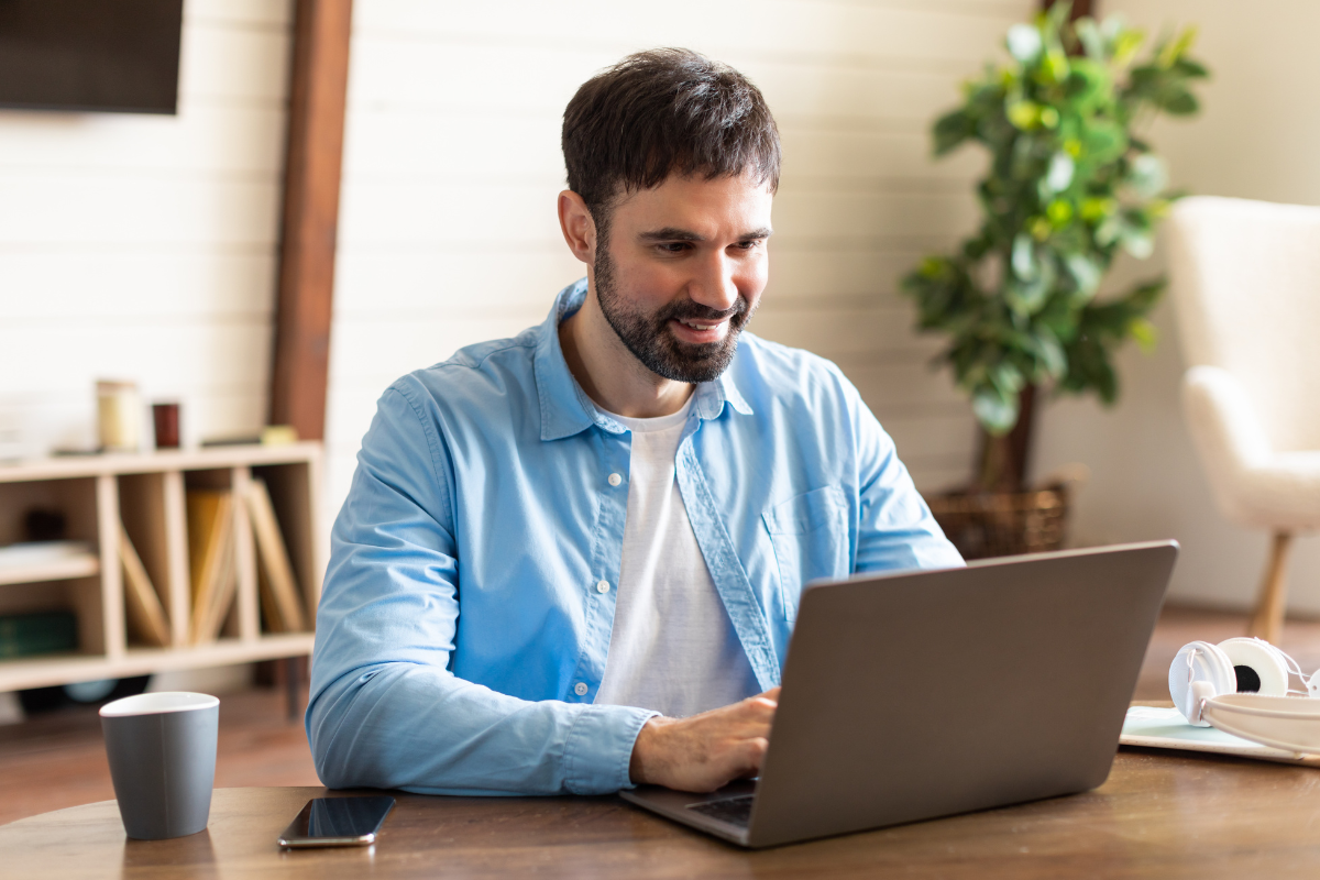 Homem sentado usando notebook sobre uma mesa com celular e xícara ao lado em ambiente de escritório representando: Rejeição 600: CSOSN incompatível na operação com Não Contribuinte.