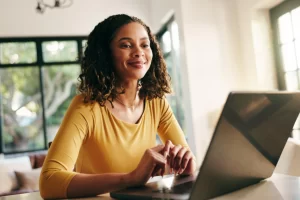 Mulher sentada usando notebook sobre uma mesa em ambiente de escritório representando: CFOP 5656: venda de combustível ou lubrificante adquirido ou recebido de terceiros destinado a consumidor ou usuário final.