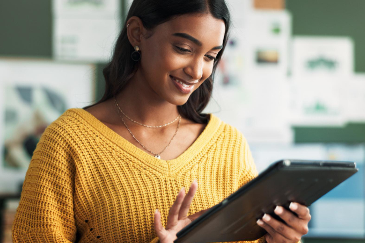 Mulher em ambiente de escritório sorridente usando tablet representando: Reforma Tributária e substituição tributária: ela vai acabar?