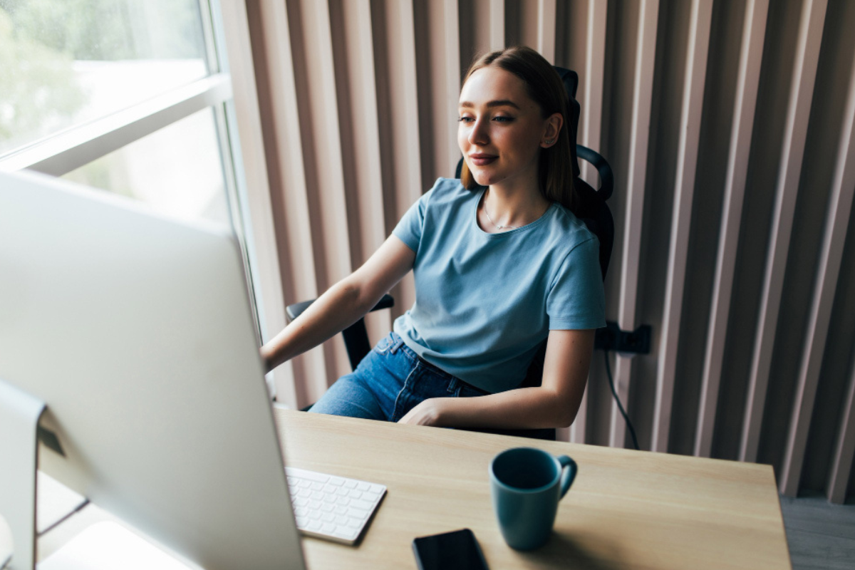 Moça sentada usando computador sobre uma mesa em ambiente de escritório home office representando: Modelo de nota fiscal com IBS e CBS: o que muda na emissão dos novos tributos.