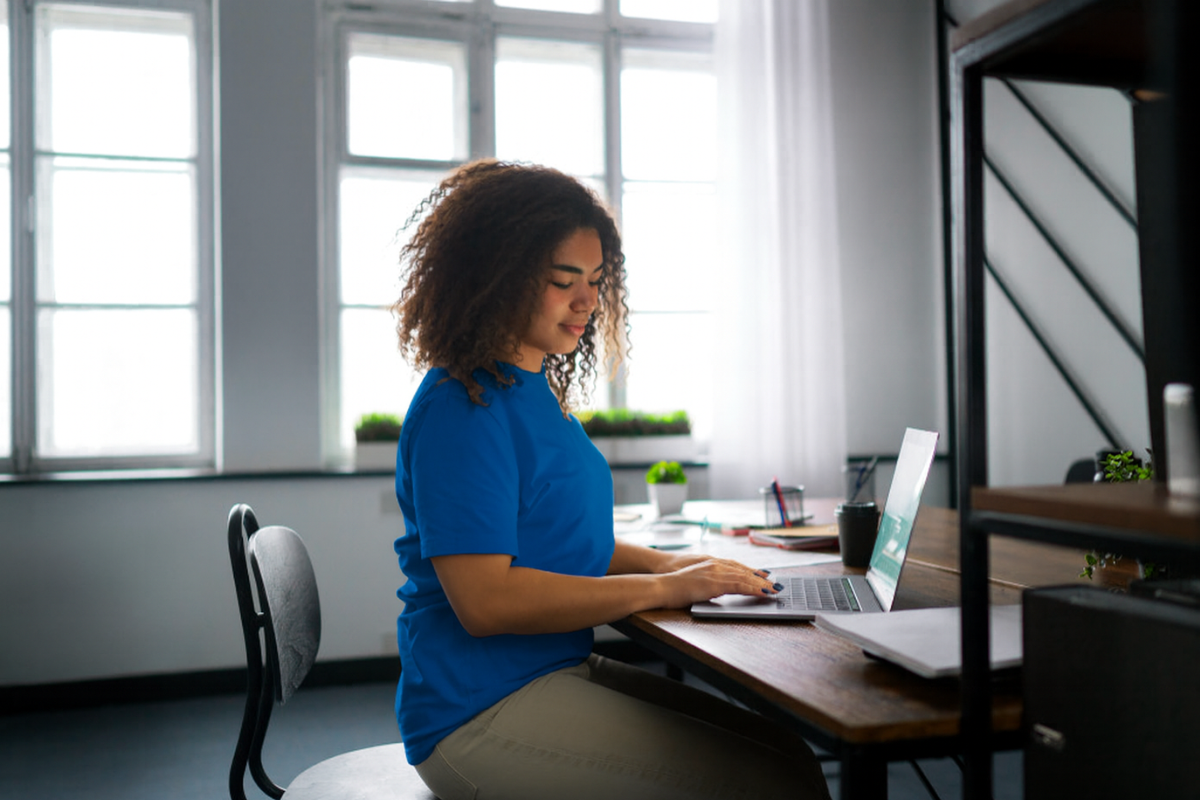Moça sentada trabalhando em um notebook sobre uma mesa em ambiente de escritório representando: Crédito Tributário: o que é e o que gera.