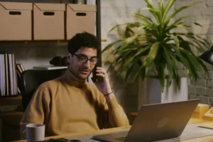 Homem sentado trabalhando em um notebook sobre uma mesa em ambiente de escritório representando: Débito Tributário: o que gera e como pagar.
