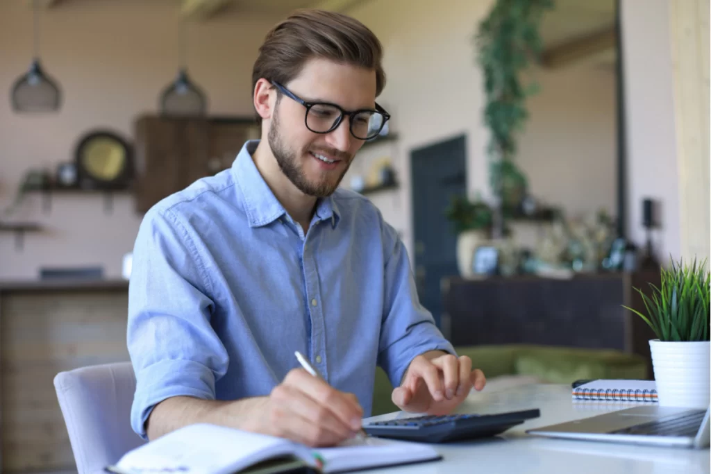 Homem em ambiente de escritório sentado em frente a um notebook usando uma calculadora e fazendo anotações representando: O que muda na NCM com a Reforma Tributária 2025?
