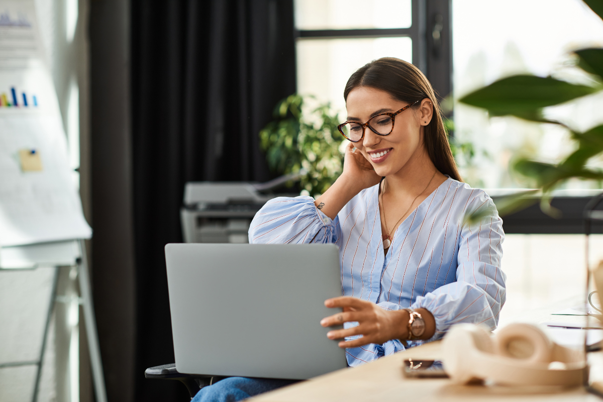 Mulher em ambiente de escritório sentada usando notebook representando: Comitê Gestor do IBS: o que é e como funcionará?