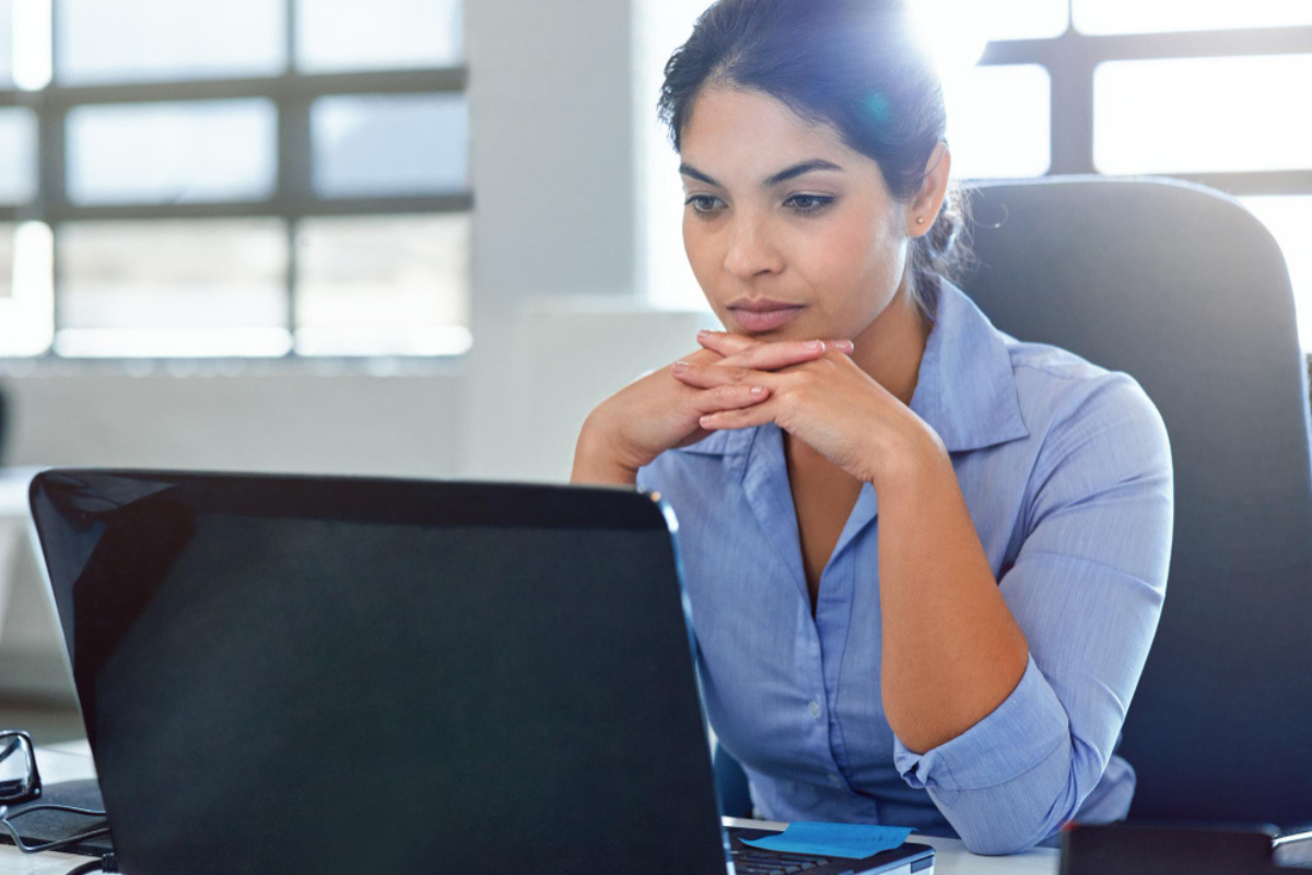 Mulher sentada usando um computador em ambiente de escritório representando: O que são obrigações acessórias?