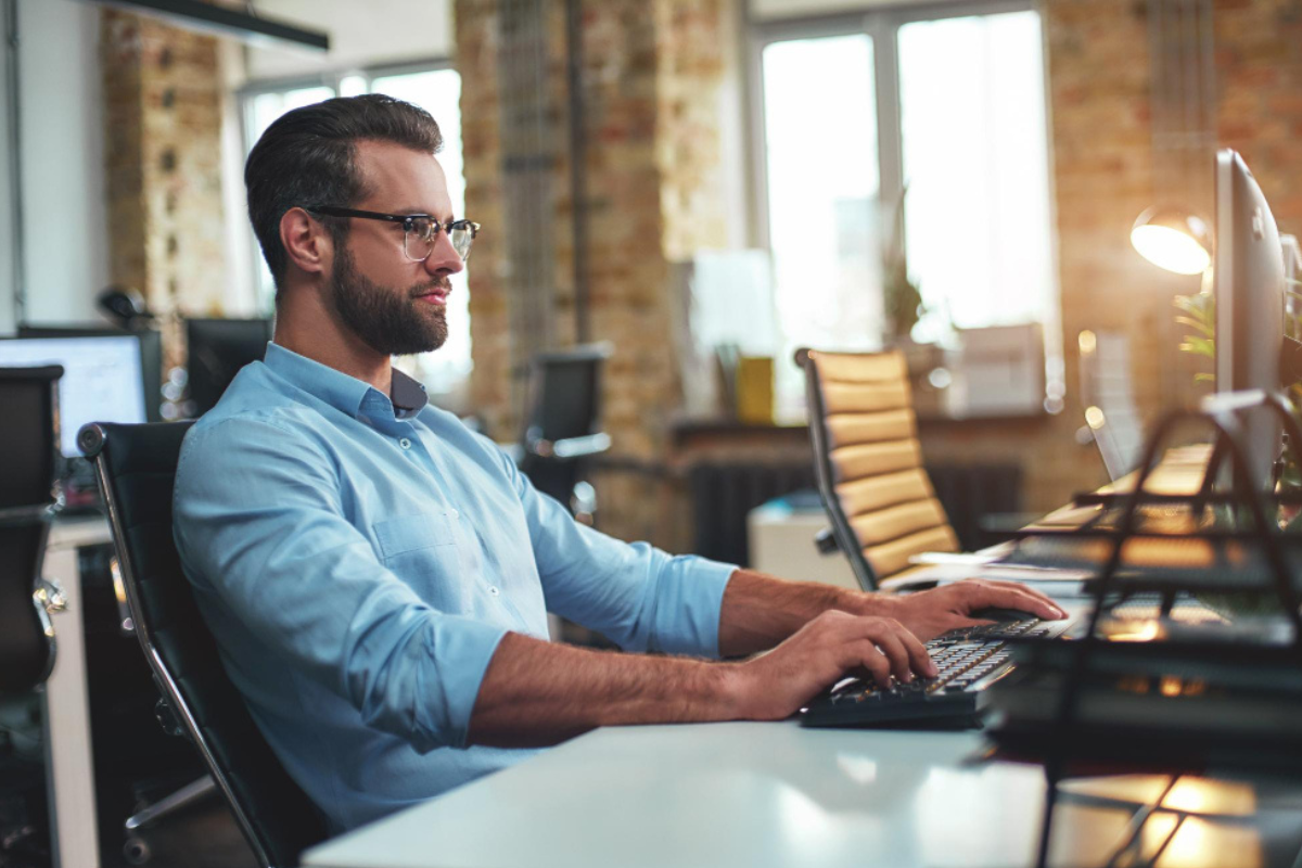 Homem em ambiente de escritório home office sentado trabalhando em um computador sobre uma mesa representando: Lucro real: tudo sobre esse regime tributário.