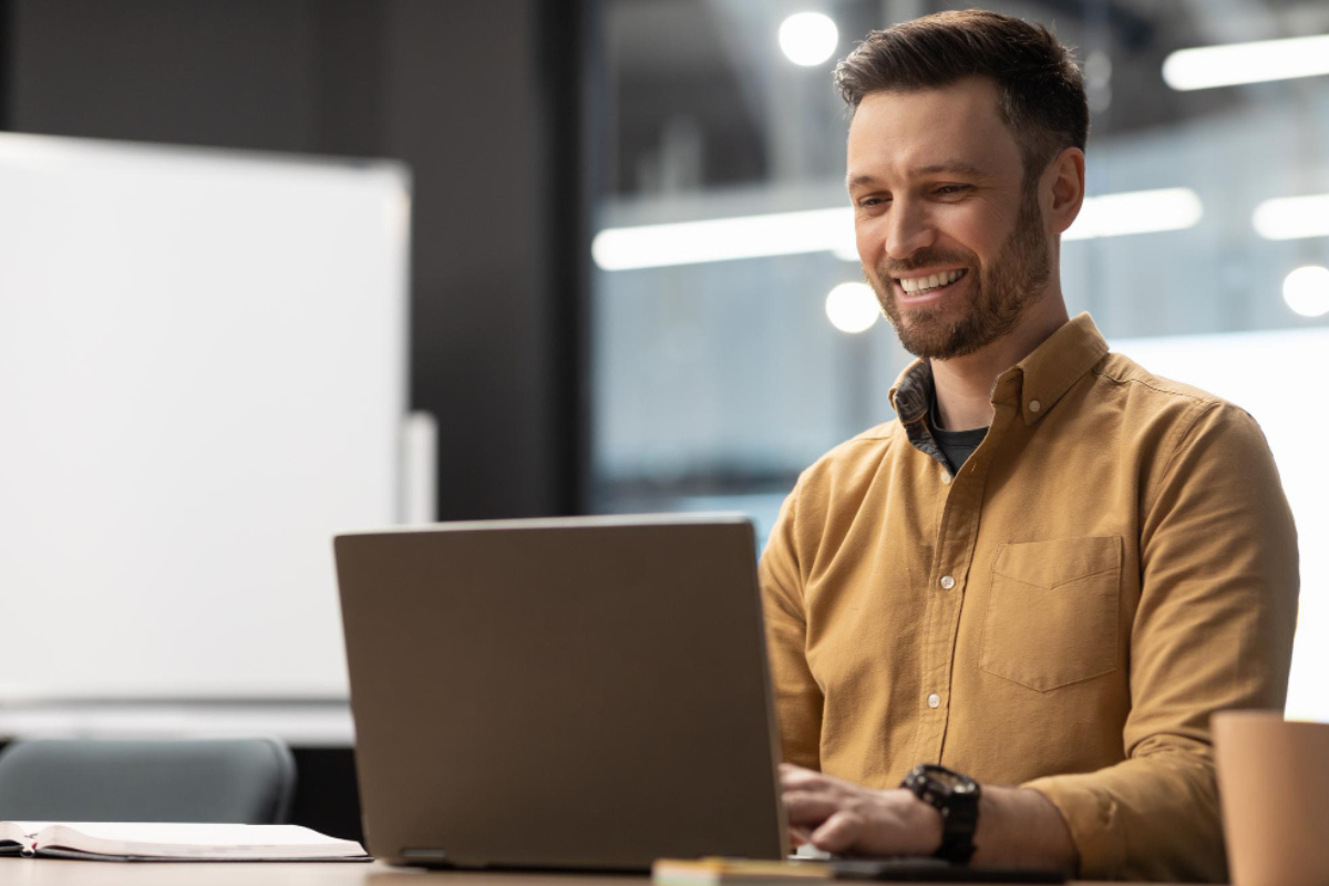 Homem sentado trabalhando em um notebook sobre uma mesa em ambiente de escritório representando: Reforma Tributária e digitalização: como a tecnologia pode ajudar na conformidade.