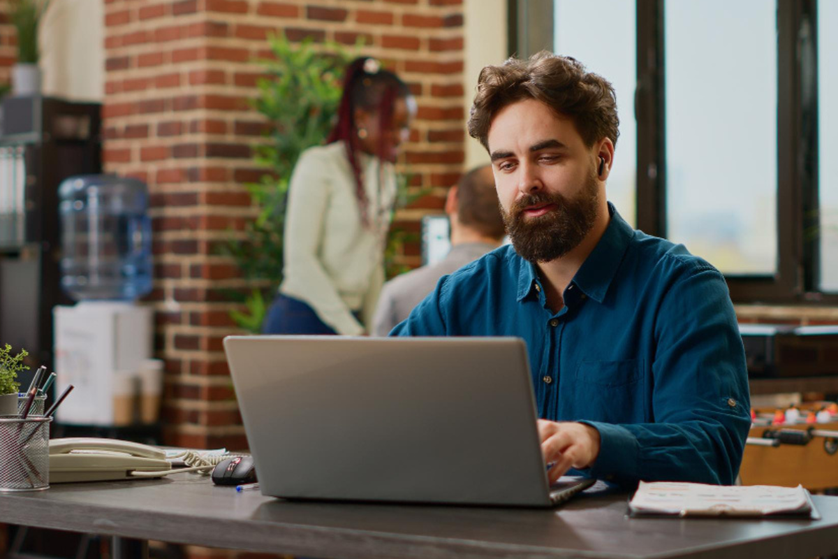 Homem sentado trabalhando em um notebook em ambiente de escritório representando: Como a CBS deve aparecer no XML?