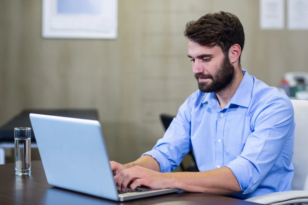 Homem em ambiente de escritório sentado usando notebook sobre uma mesa representando: Por que a NF-e é essencial para a apuração de tributos.