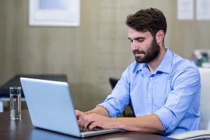 Homem em ambiente de escritório sentado usando notebook sobre uma mesa representando: Por que a NF-e é essencial para a apuração de tributos.