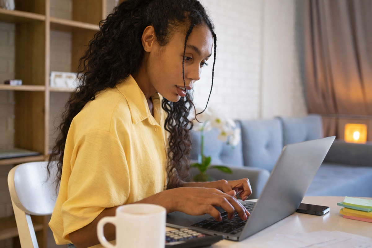 Mulher trabalhando em um notebook sobre uma mesa em ambiente de escritório representando: Rejeição 629: Valor do Produto difere do Valor Unitário de Comercialização e Quantidade Comercial.