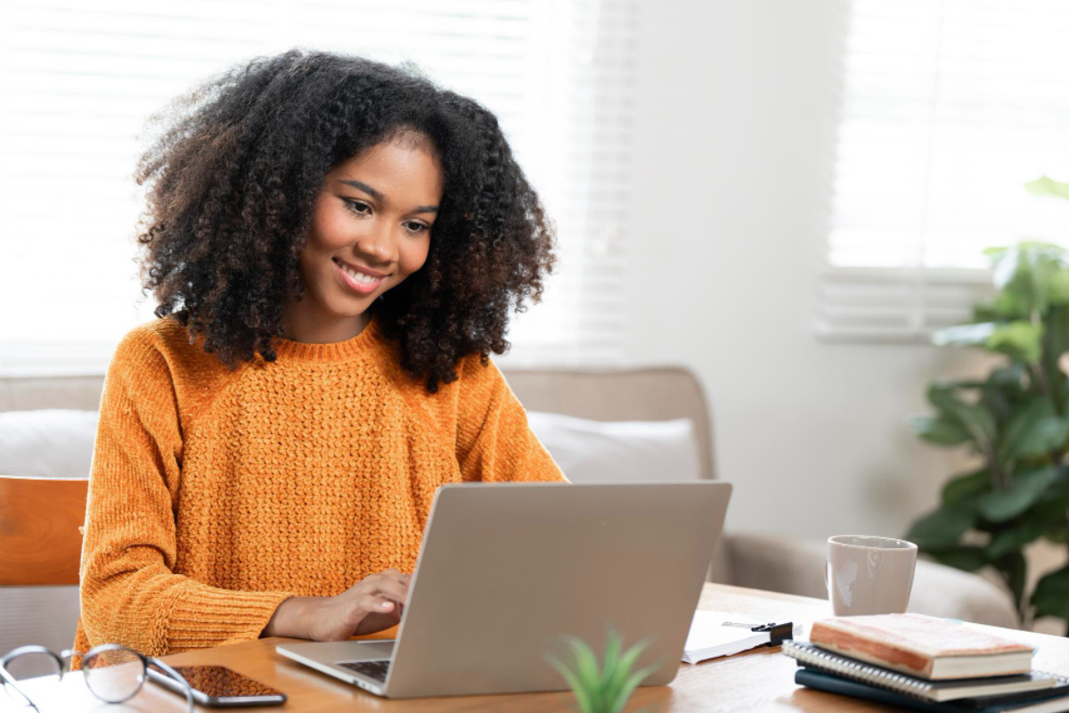 Mulher trabalhando em um notebook sobre uma mesa em ambiente de escritório representando: Reforma Tributária e notas de serviço: o fim do ISS muda o quê na NFS-e?