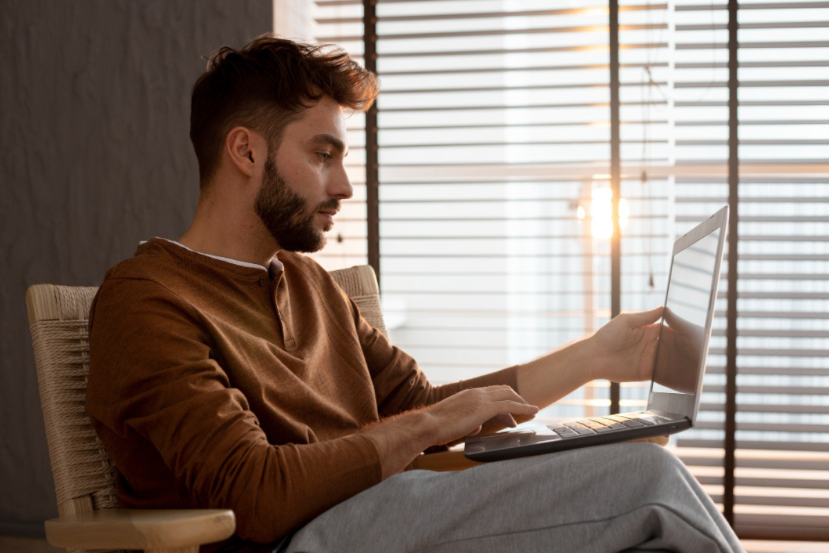 Homem sentado em poltrona usando notebook no colo em ambiente home office representando: Imposto Seletivo na nota fiscal: quem precisa destacar e como funciona.