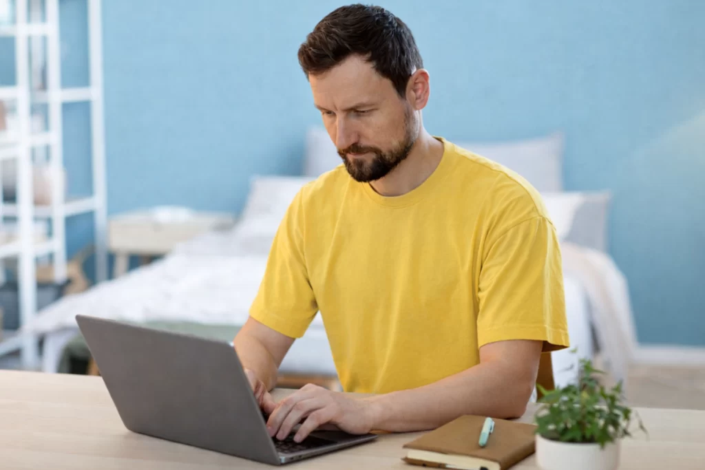 Homem sentado trabalhando em um notebook em ambiente home office representando: Como emitir Nota Fiscal de Produto (NF-e) durante a transição da Reforma Tributária?