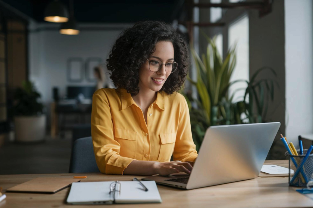 Mulher trabalhando em um notebook sobre uma mesa em ambiente de escritório representando: Como a microempresa deve emitir nota fiscal em 2026?