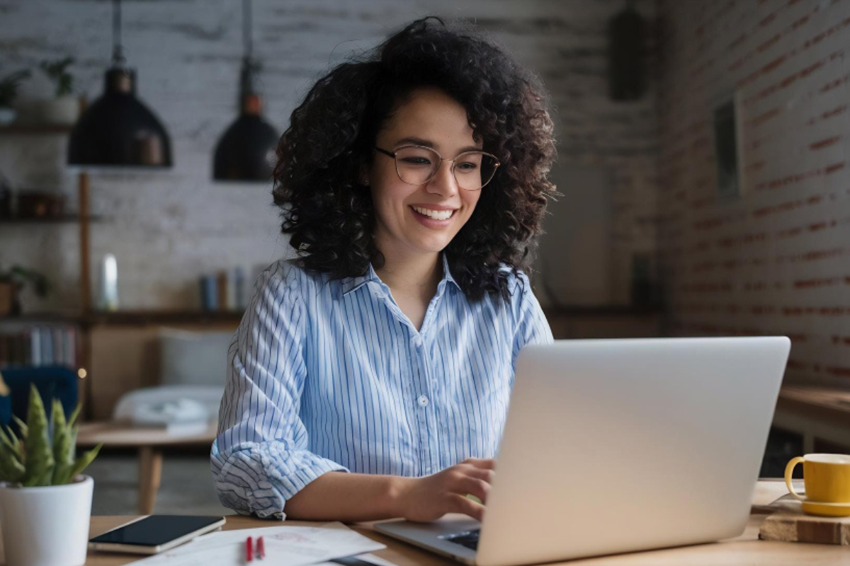 Mulher trabalhando em um notebook sobre uma mesa em ambiente de escritório representando: CFOP 6949: outra saída de mercadoria ou prestação de serviço não especificado.