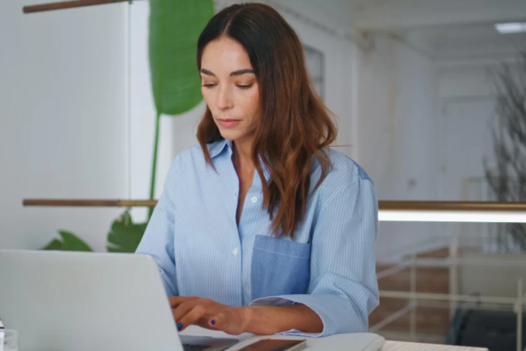 Mulher trabalhando em um notebook sobre uma mesa em ambiente de escritório representando: CFOP 5910: remessa em bonificação, doação ou brinde.