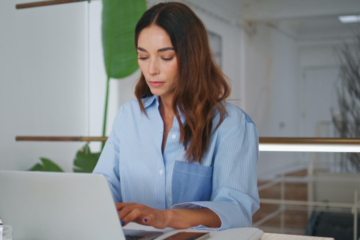Mulher trabalhando em um notebook sobre uma mesa em ambiente de escritório representando: CFOP 5910: remessa em bonificação, doação ou brinde.