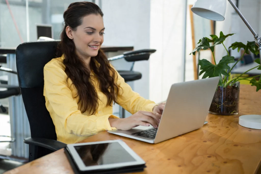 Mulher trabalhando em um notebook sobre uma mesa em ambiente de escritório representando: CFOP 6201: devolução de compra para industrialização.