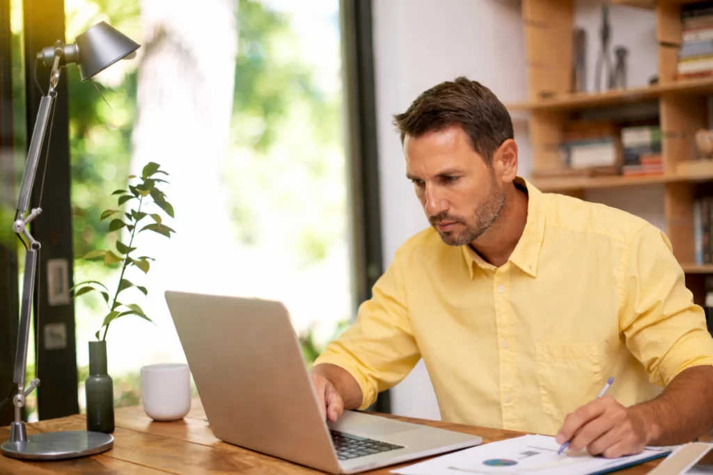 Homem sentado trabalhando em um notebook em ambiente home office representando: Indicadores contábeis que o empresário deveria acompanhar.