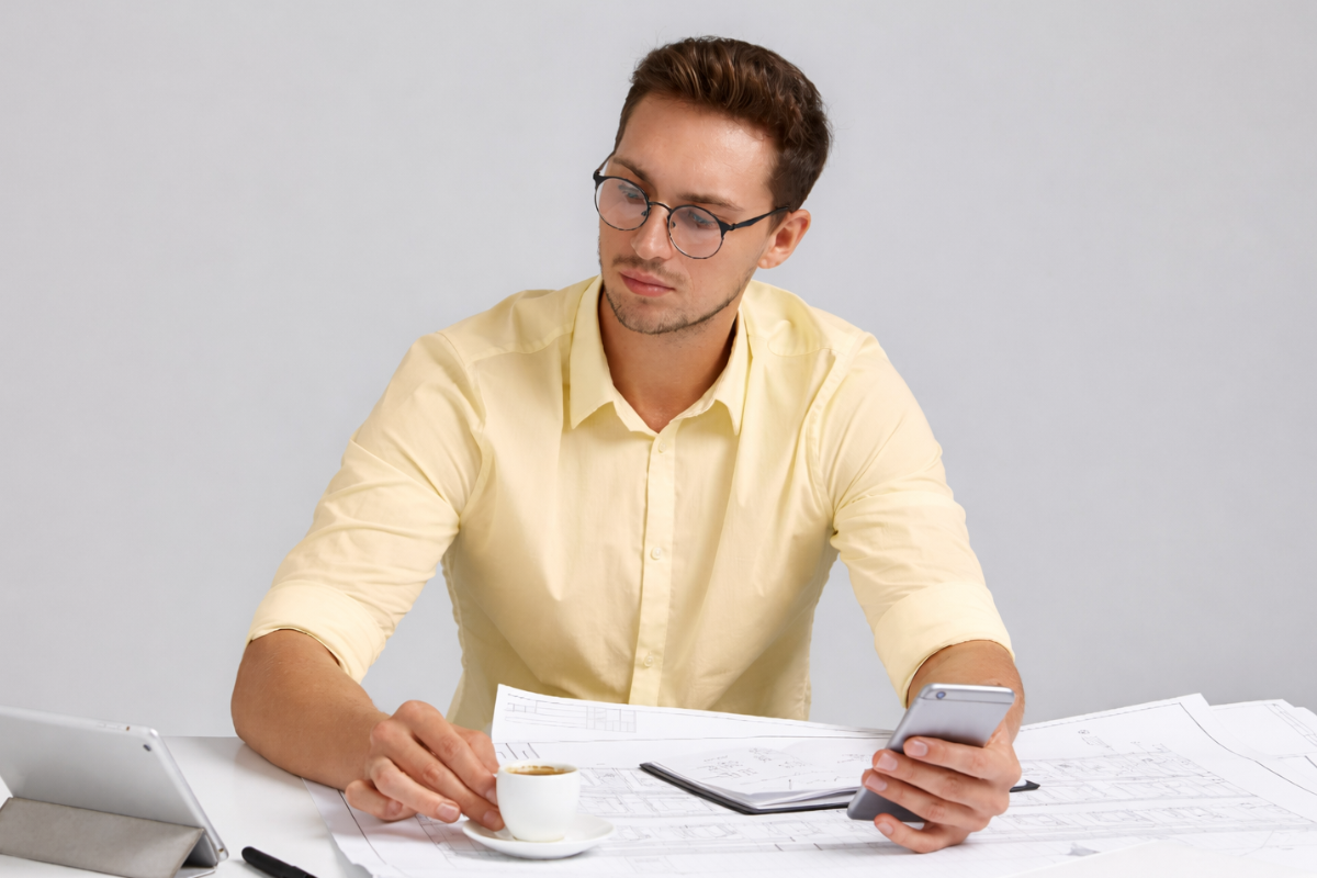 Homem sentado fazendo anotações em uma agenda sobre uma mesa e usando celular, com uma xícara de café ao lado em ambiente de escritório representando: Quando a empresa pode ser excluída do Simples por irregularidade fiscal?