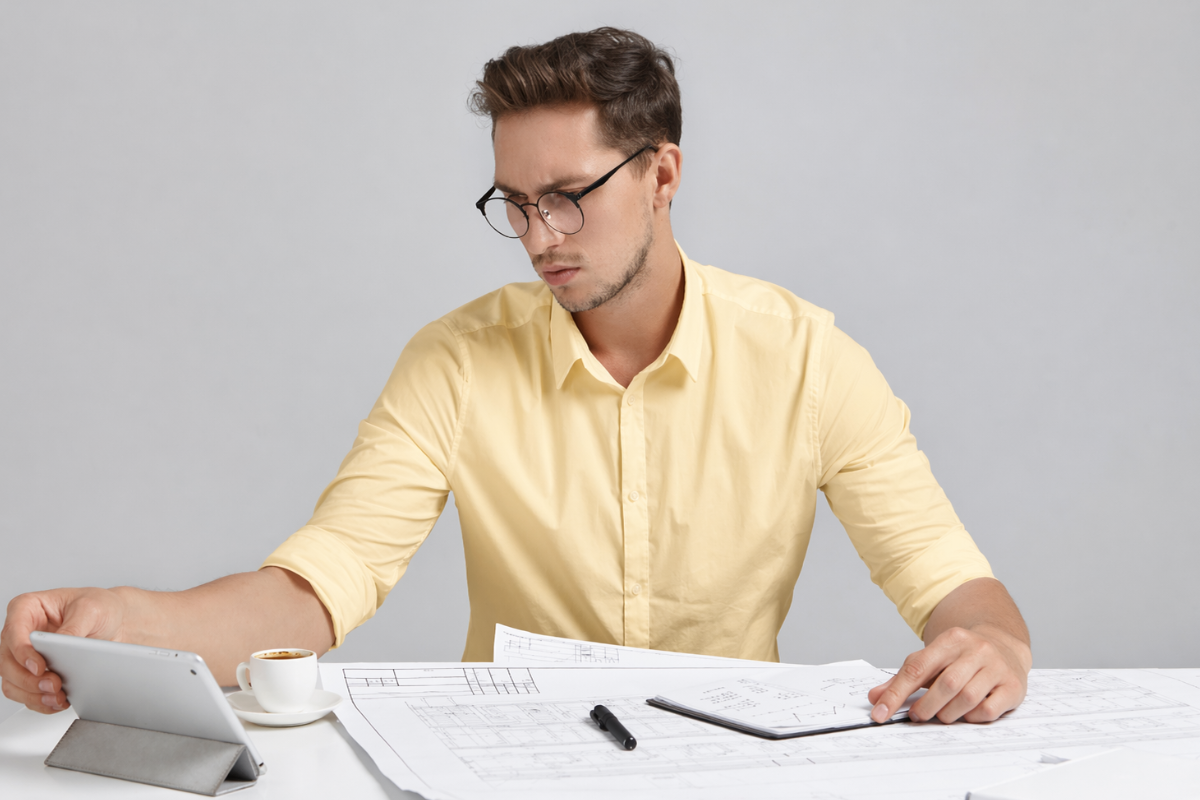 Homem sentado usando um tablet sobre uma mesa e fazendo anotações em agenda em ambiente de escritório representando: CFOP 3949: outra entrada de mercadoria ou prestação de serviço não especificado.