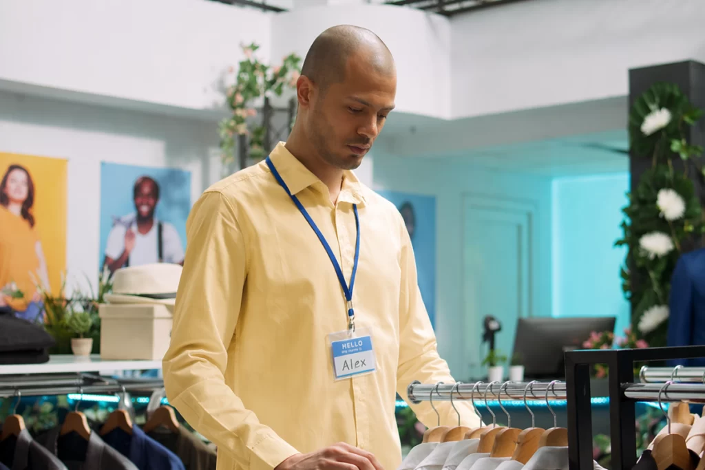 Homem funcionário de uma loja de roupas arrumando exposição de roupas masculinas em seu ambiente de trabalho representando: CFOP 1914: retorno de mercadoria ou bem remetido para exposição ou feira.