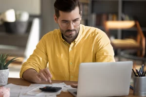 Homem sentado trabalhando em um notebook em ambiente home office representando: Valor aproximado dos tributos: como calcular e aplicar corretamente.