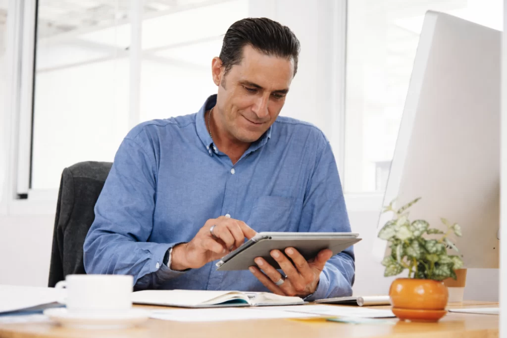 Homem sentado trabalhando em um tablet em ambiente home office representando: Erros comuns no Simples Nacional na emissão de nota fiscal.