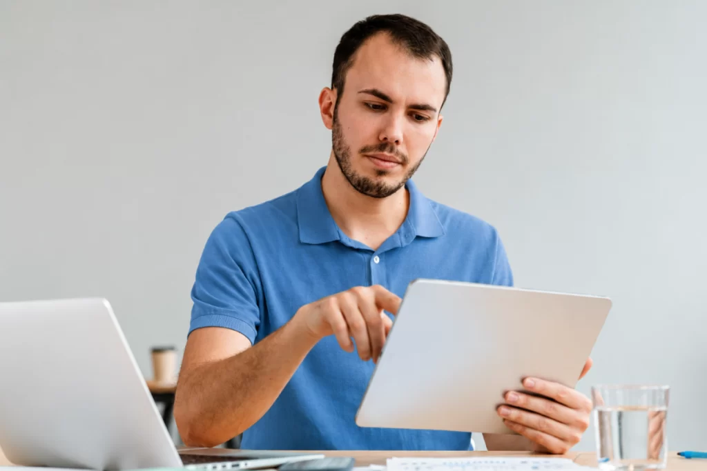 Homem em ambiente de escritório sentado lendo documentos ao lado de um notebook sobre Como preparar SPED para o novo modelo tributário.