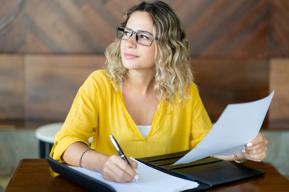 Empreendedora feminino trabalhando em seu notebook, fazendo anotações e analisando documentos representando: Regime de competência e emissão de notas fiscais: muda alguma coisa?