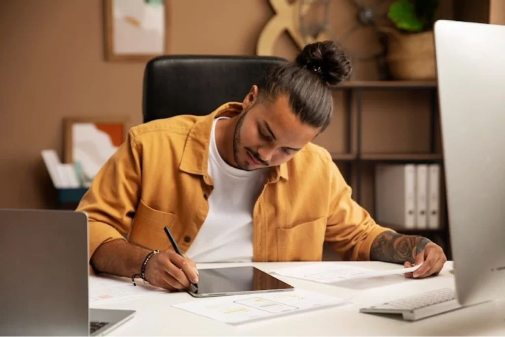 Home de vista frontal trabalhando sentado, usando um tablet, um computador e um notebook sobre a mesma mesa representando: Escrituração fiscal digital para contadores autônomos: obrigações e ferramentas.