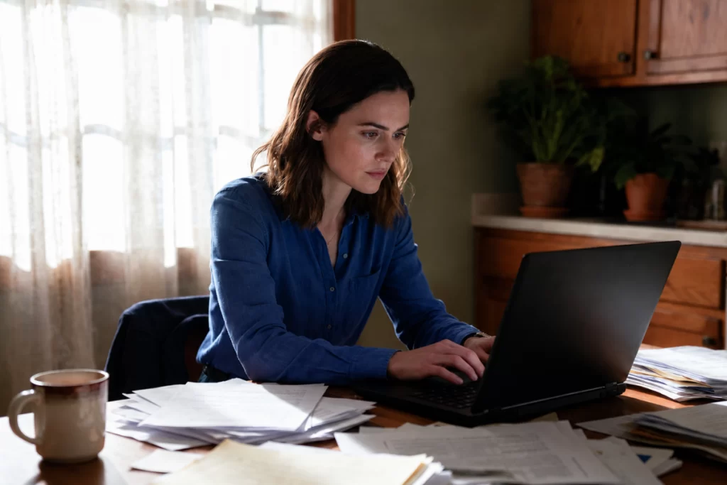 mulher em seu escritório pensativa e teclando em seu notebook que está sobre a mesa, representando: Nota fiscal complementar: quando é obrigatória?