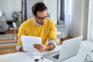 Empreendedor sentado sobre a mesa comparando conteudo do papel e notebook, representando: O que acontece se sua empresa parar de emitir notas?