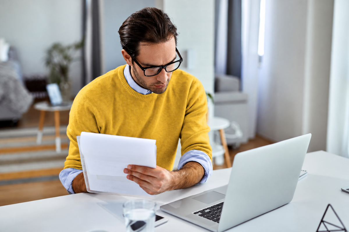 Empreendedor sentado sobre a mesa comparando conteudo do papel e notebook, representando: O que acontece se sua empresa parar de emitir notas?