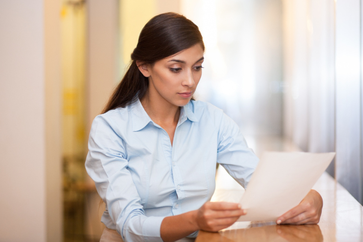 Mulher centada a mesa analisando um folha de papel, representando: Documentação fiscal: o que a empresa precisa guardar