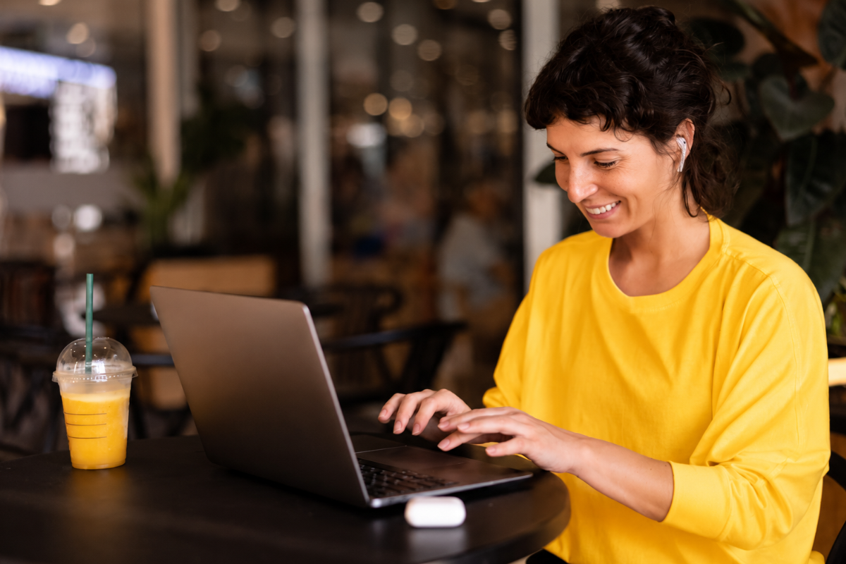 Mulher sentada em uma mesa de restaurante com seu notebook, representando: Split payment na Reforma Tributária: quem recolhe o IBS e CBS e o que muda para a microempresa